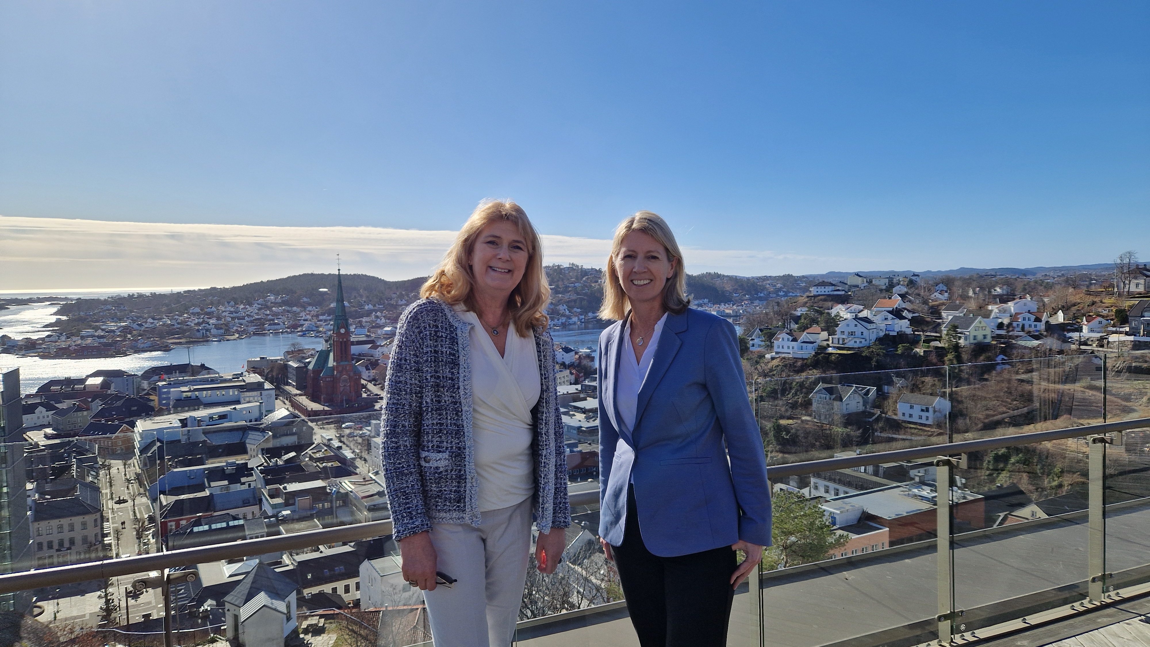 To smilende mennesker stående ved siden av hverandre, med utsikt over Arendal i bakgrunnen