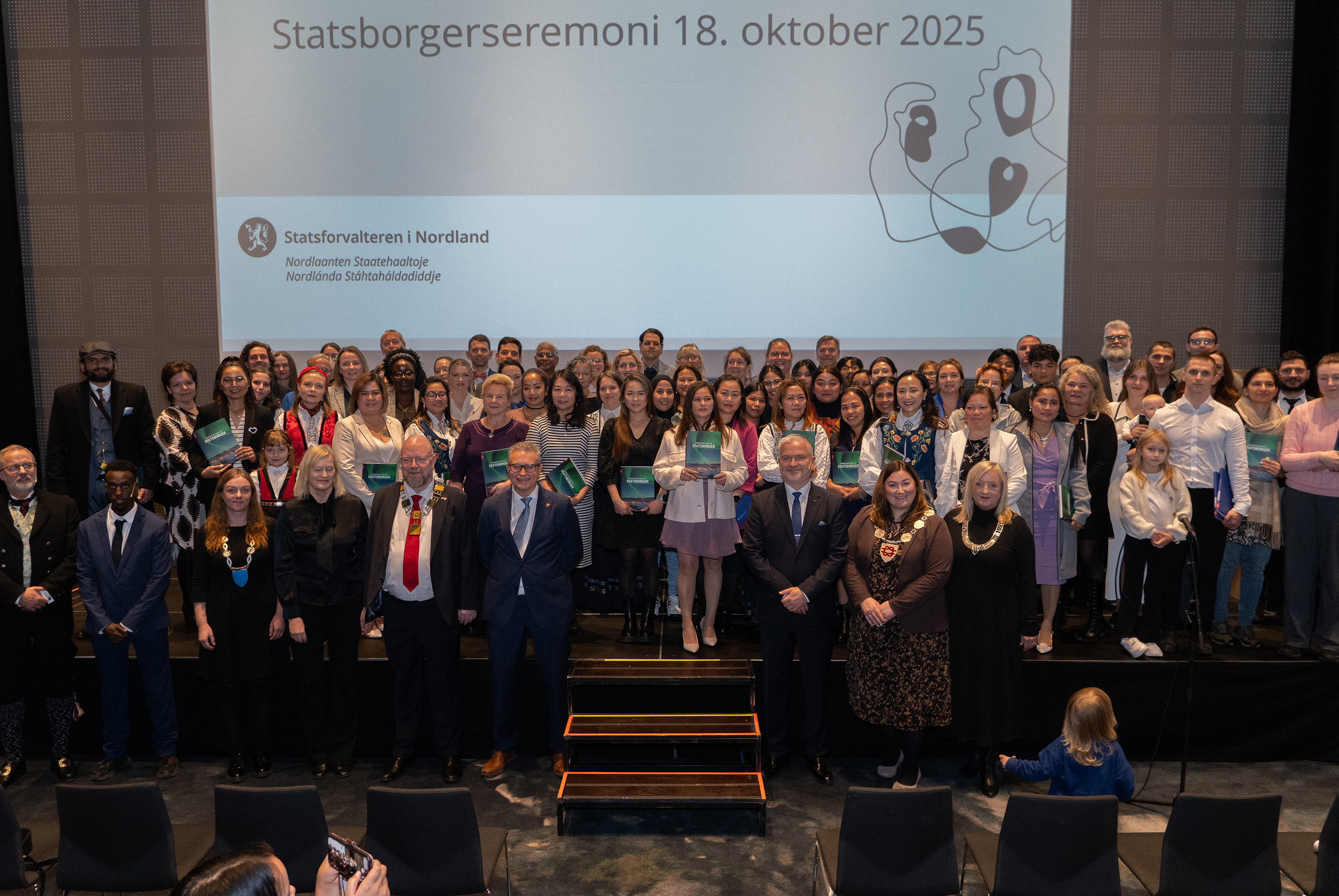 Govven: Emil Harjo Indsetviken / Statsforvalteren i Nordland. En stor gruppe pent kledde mennesker står oppstilt på en scene.