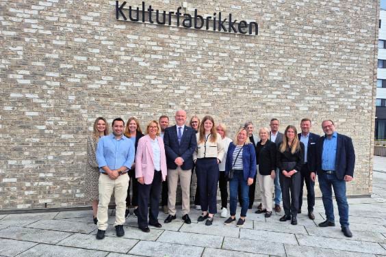 En gruppe mennesker står oppstilt foran en lys murvegg.