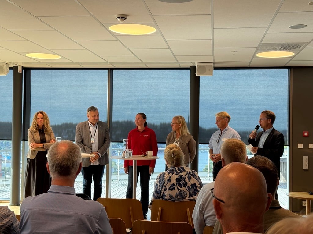 Seks deltakarar står framme i eit møterom under ein paneldebatt om beredskap og totalforsvar. Publikum sit på stolrekkjer framfor panelet, med store vindauge i bakgrunnen.