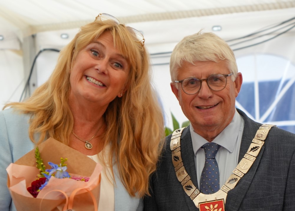Smilende kvinne med blomster i hånden, og smilende mann med ordførerkjede