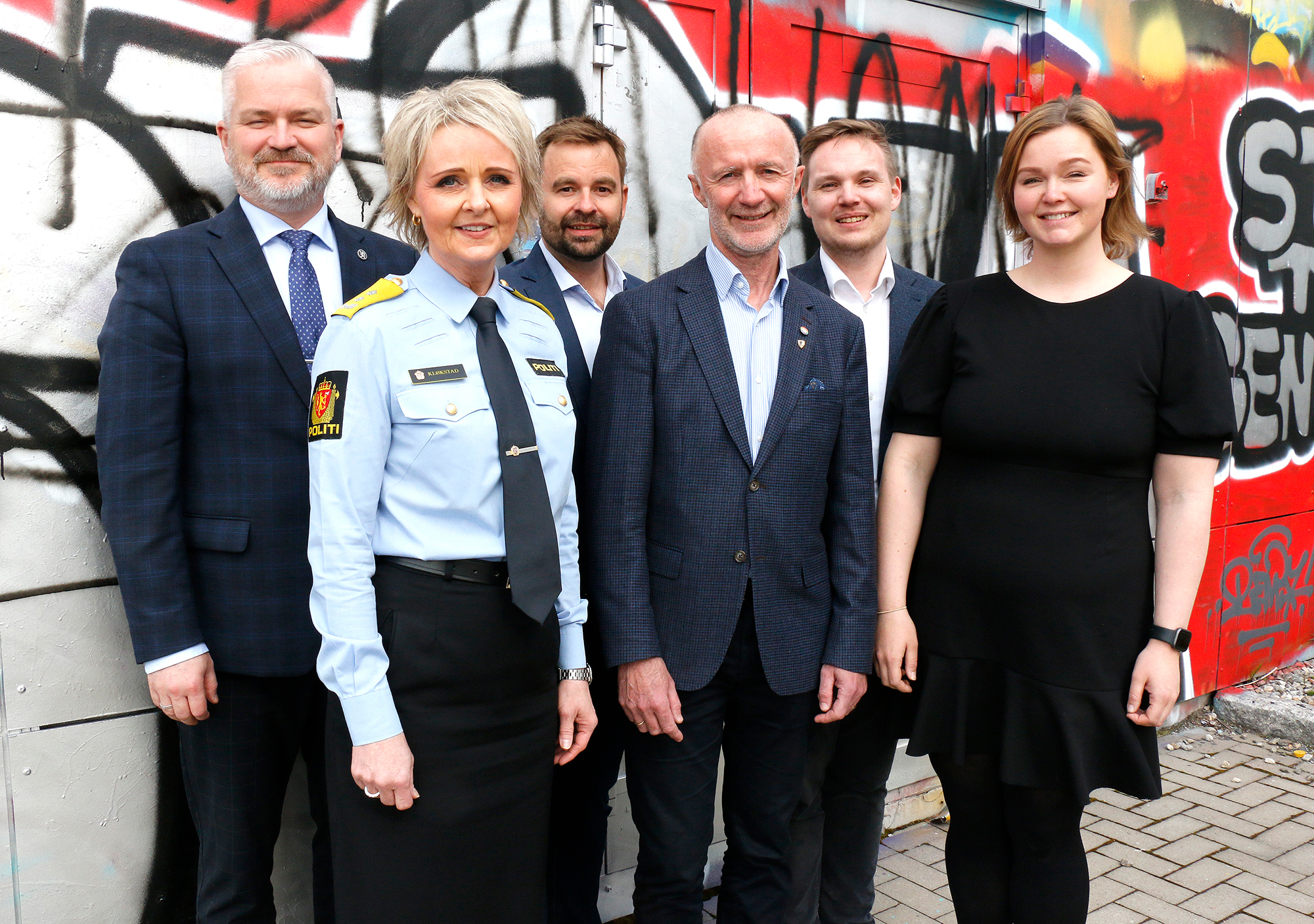 Fra venstre statsforvalter Tom Cato Karlsen, politimester i Nordland Heidi Kløkstad, daglig leder i Salten regionråd Allan Ellingsen, fylkesrådsleder Sven Eggesvik, fylkesråd for utdanning Joakim Sennesvik og Aina Nilsen, som er fylkesråd for finans og organisasjon. Foto: Trond-Erlend Willassen / Nordland fylkeskommune. Fire menn i mørk dress, en kvinne med mørk kjole og en kvinne med blå skjorte og sort skjørt står utendørs foran en fargerik vegg.