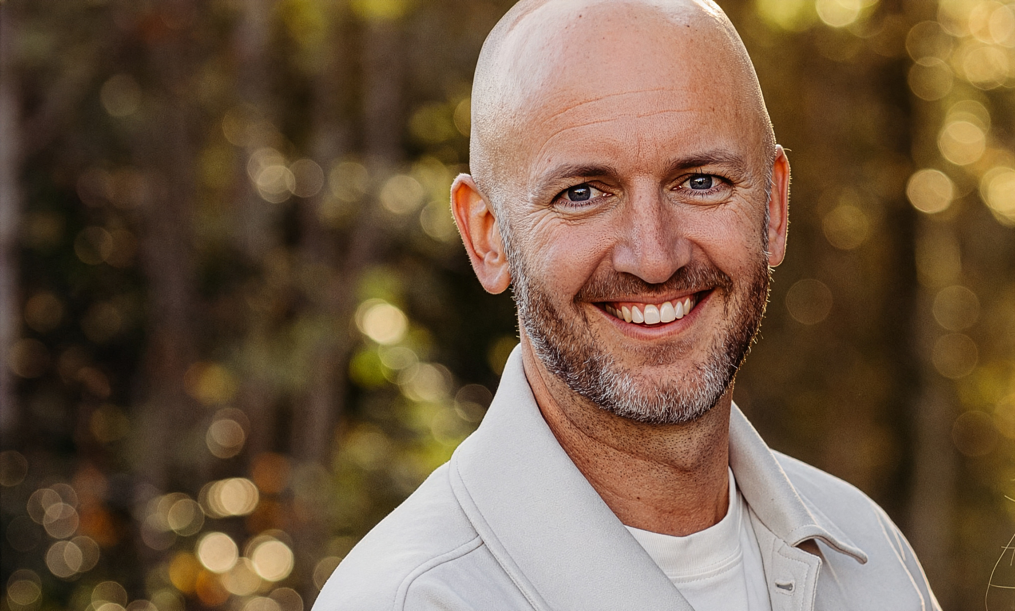 Person i lyse klede står utandørs framfor solbelyste tre