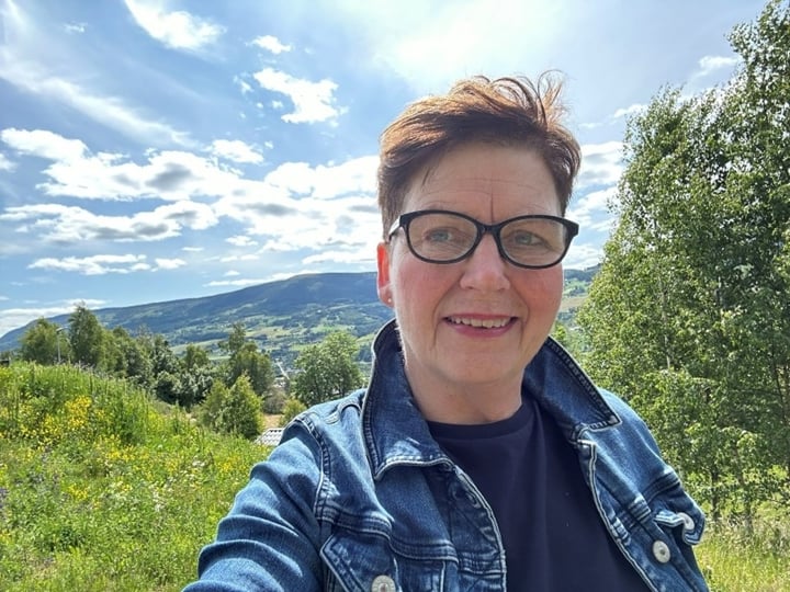 Eli Blakstad er tilbake hos Statsforvalteren i Innlandet etter å ha vært statssekretær, og leder nå arbeidet med klima, landbruk og naturforvaltning. Foto: Eli Blakstad / Eli Blakstad. Eli Blakstad i nærbilde, i grønne landskap i Gudbrandsdalen.