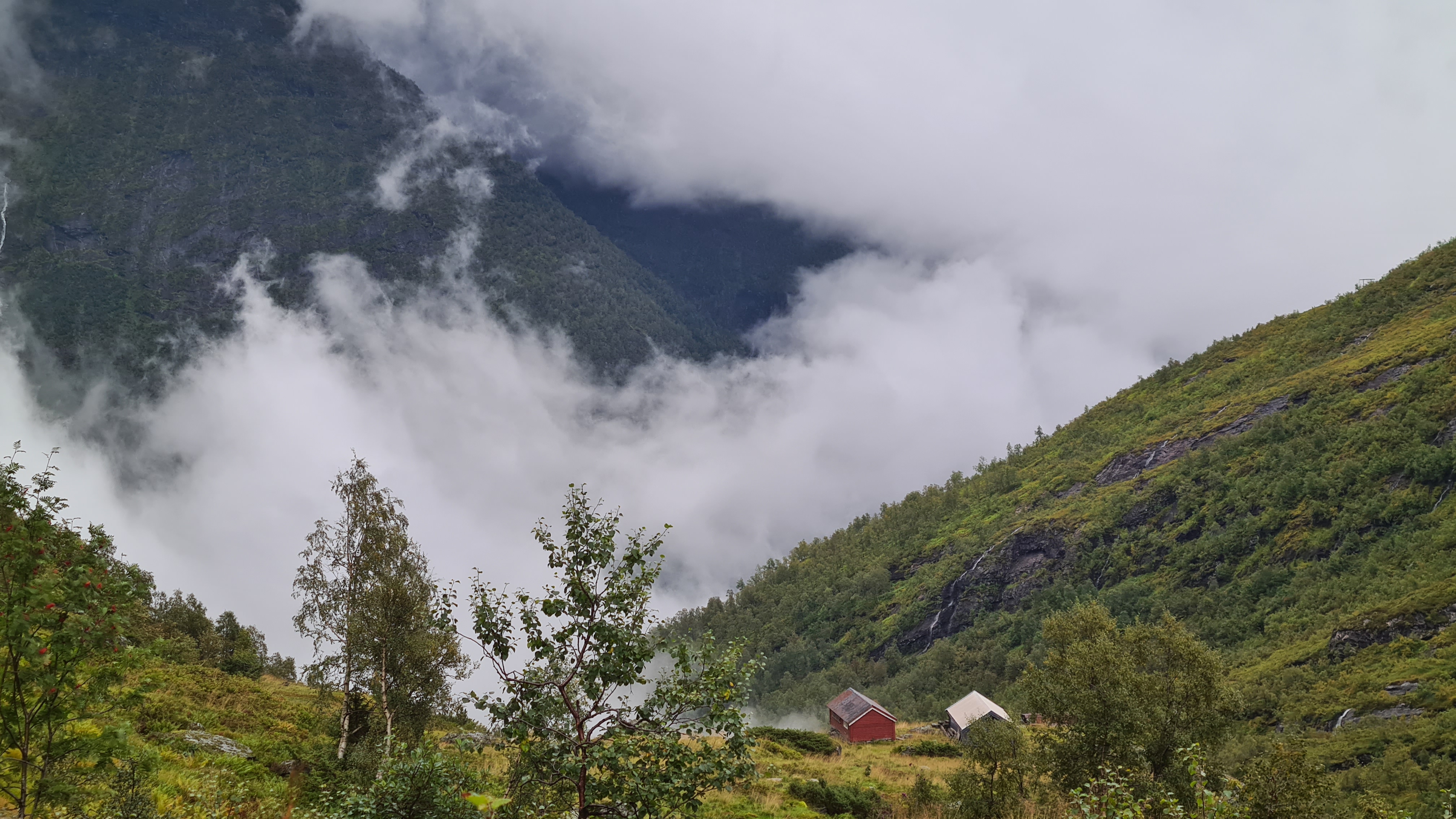 to stølshus i forgrunnen og fjell i tåkelandskap i bakgrunnen