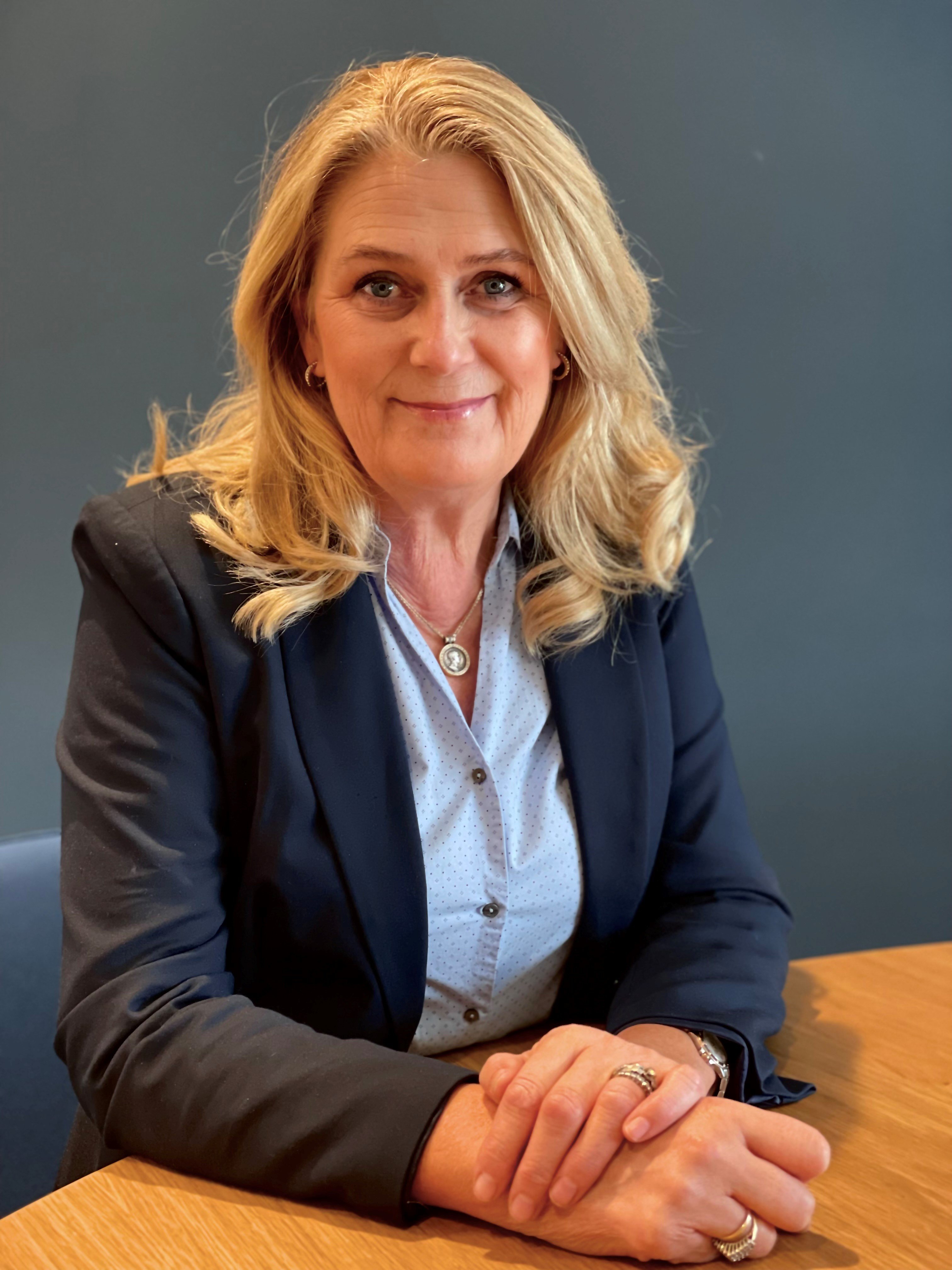 En smilende kvinne som sitter ved et rundt bord.