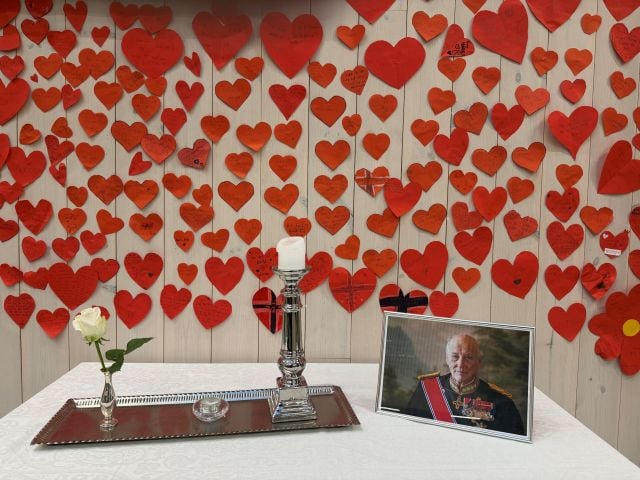 Røde papirhjerter henger over et bord med lys og bilde av Kong Harald.