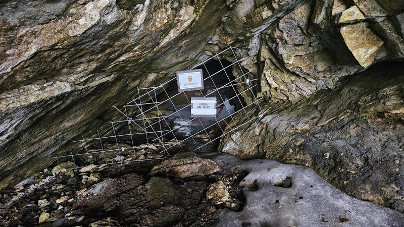 Nærbilde av et hull i en bergvegg. Hullet er sperret av et metallgjerde.