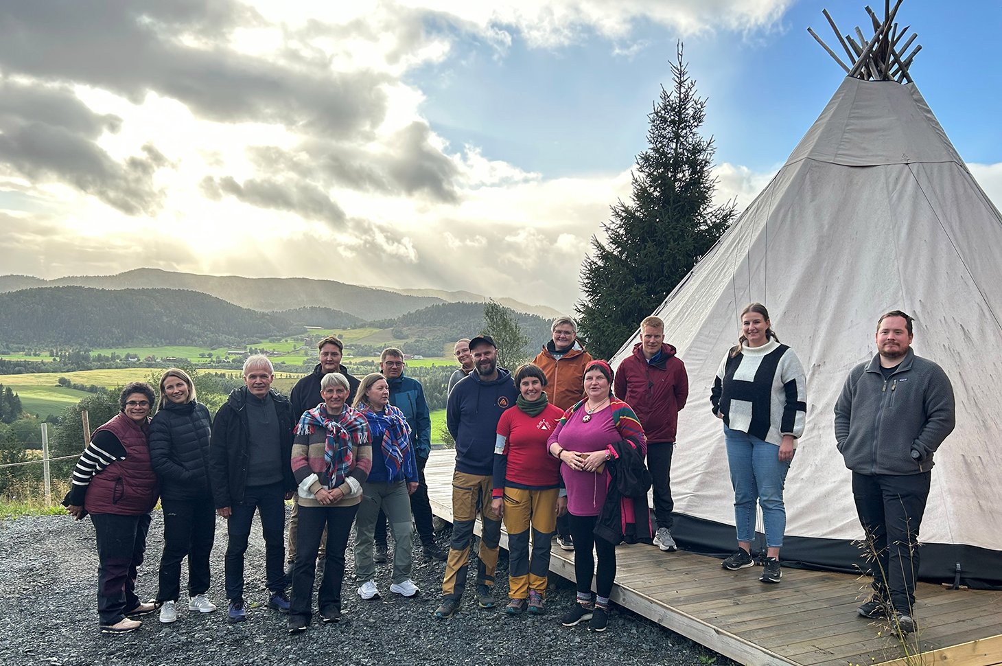 Deltakerne var blant annet på besøk hos Aejrie Sïjte på Namdalseid i Trøndelag. Foto: Ingrid Roaldsen / Statsforvalteren i Nordland. En gruppe mennesker står ved siden av en lavvo med grønne jorder og åser i bakgrunnen.