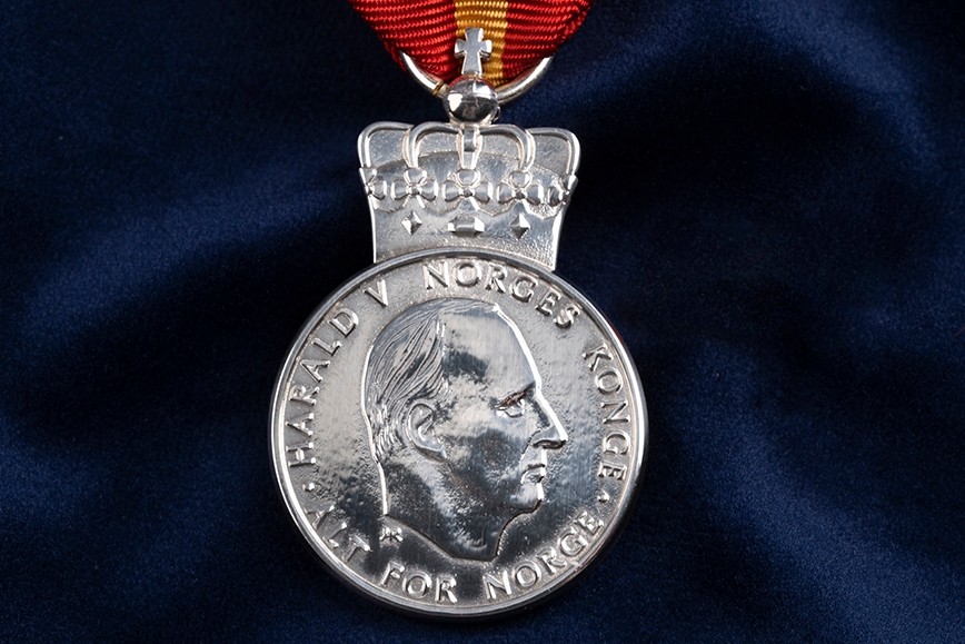 En rund sølvfarget mynt med et ansikt inngravert.