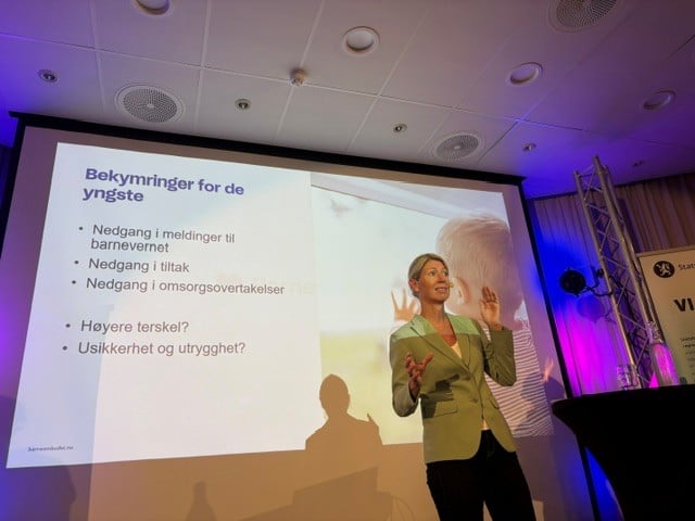 Person holder foredrag på en konferansescene foran et lysbilde om bekymringer knyttet til nedgang i meldinger, tiltak og omsorgsovertakelser i barnevernet.