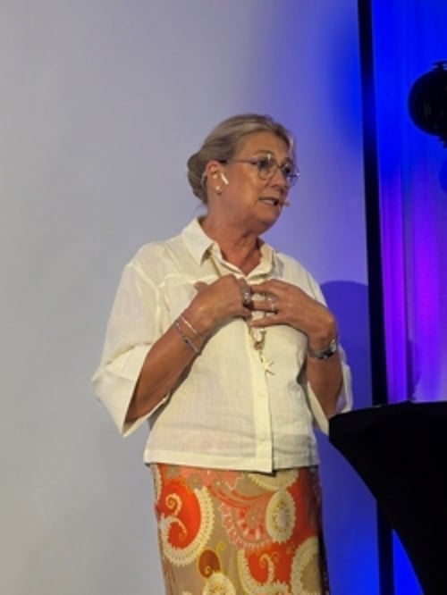 Statsforvalter Gina Lund står på en scene og holder innlegg under et seminar. Bildet er tatt foran en presentasjonsskjerm og scenebelysning i blå og lilla toner. Lund innleder seminaret om forebygging av vold og overgrep mot barn og unge under Arendalsuka.