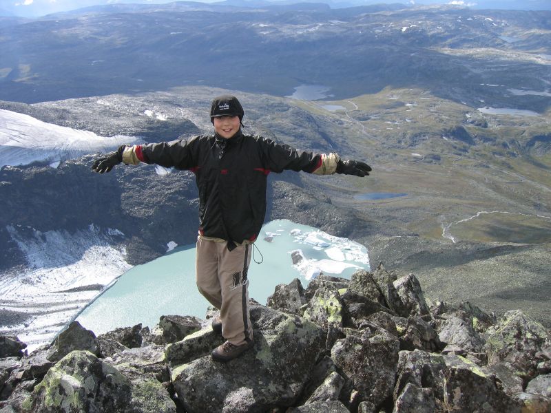 Gutt som står med utstrakte armer på et snøkledd fjell
