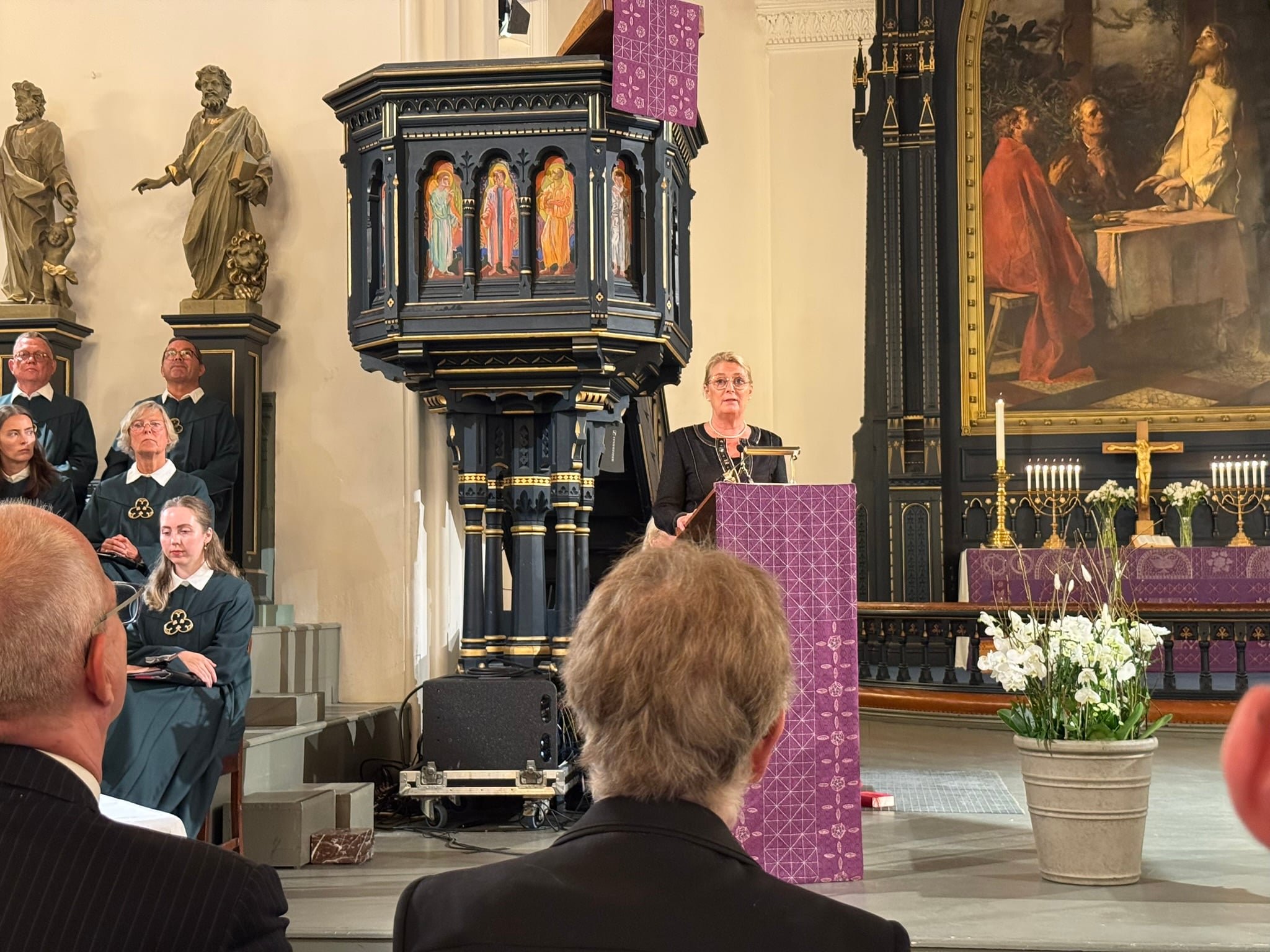 En person holder tale fra prekestolen i en kirke under en minnemarkering. Flere deltakere er samlet i kirkerommet, og alteret med lys og blomster er synlig i bakgrunnen.