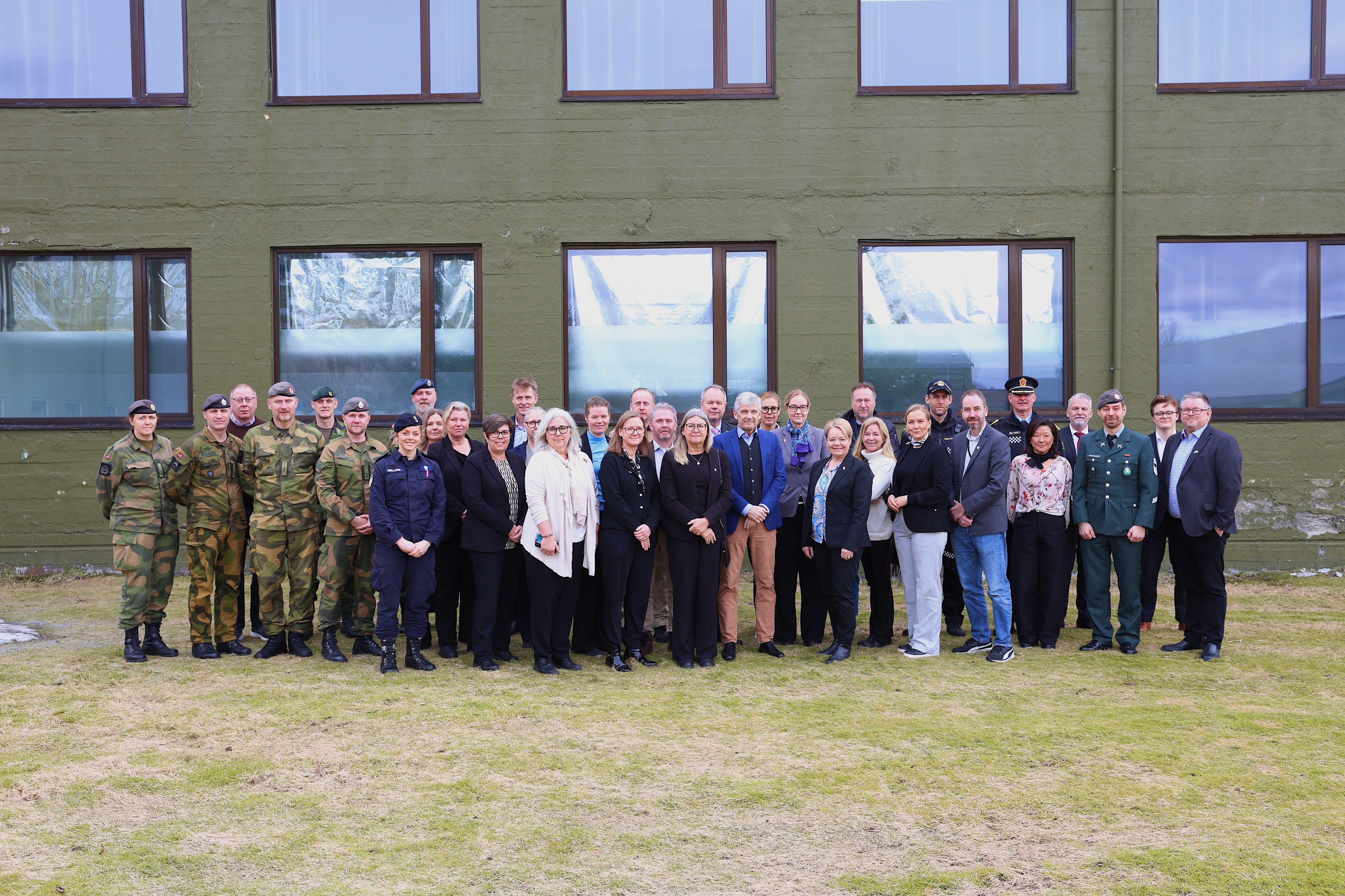 Flokk med mennesker på en plen foran en bygning. 