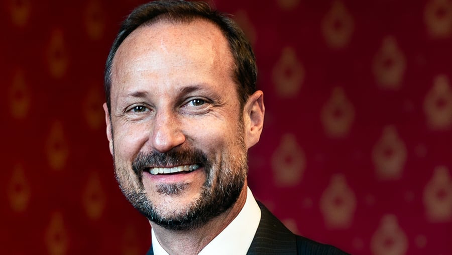 Nært portrett av kronprins Haakon, smilande og kledd i mørk dress og kvit skjorte. 