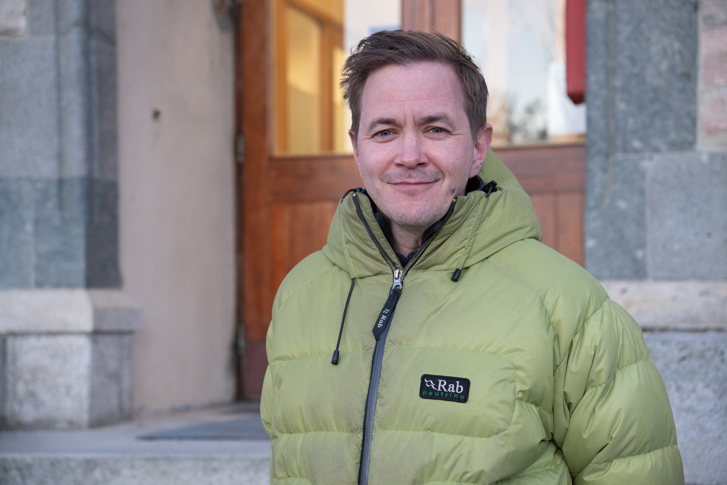 En mann med grønn jakke står foran en dør.