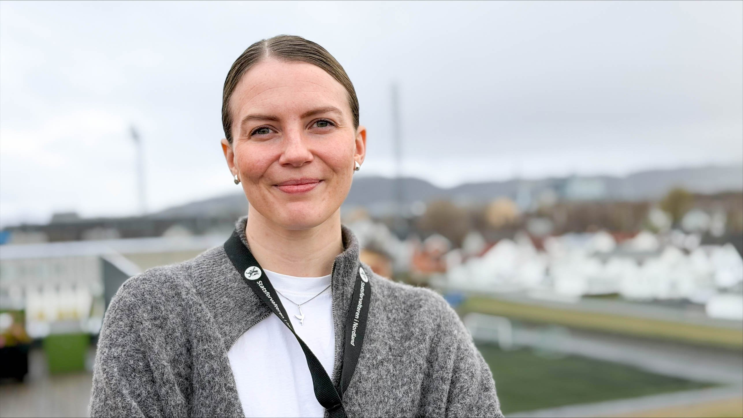 En dame som ser i kameraet. Mørkt hår. Grå genser over en hvit t-skjorte. 