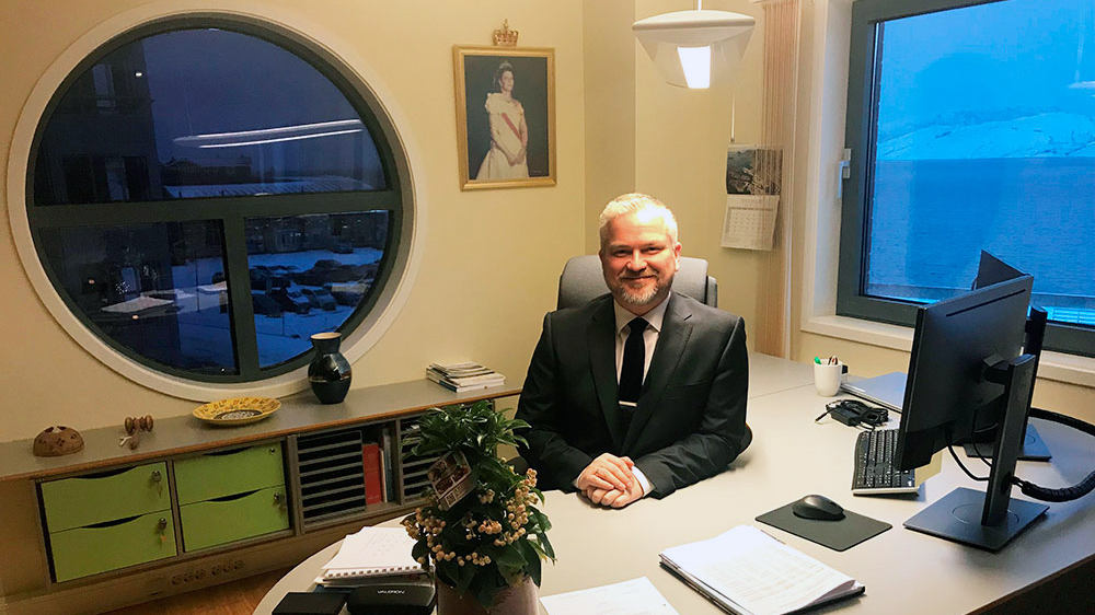 Tom Cato Karlsen tiltrådte som statsforvalter i Nordland 2. januar 2019. Nå er han utnevnt til en ny åremålsperiode på seks år. Mann i dress sitter bak skrivebord på kontor.