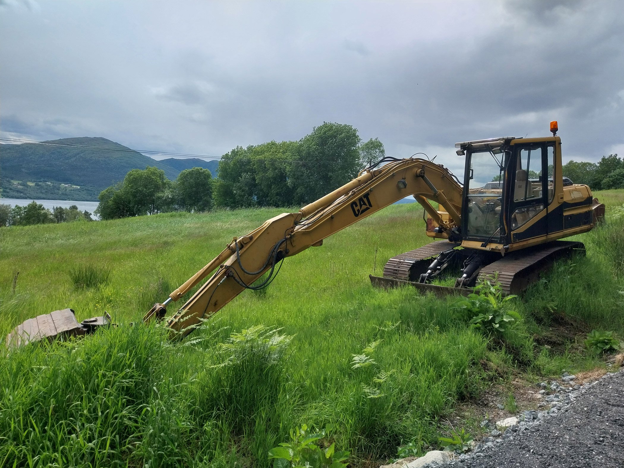 Ei gravemaskin står i ei grøn eng.