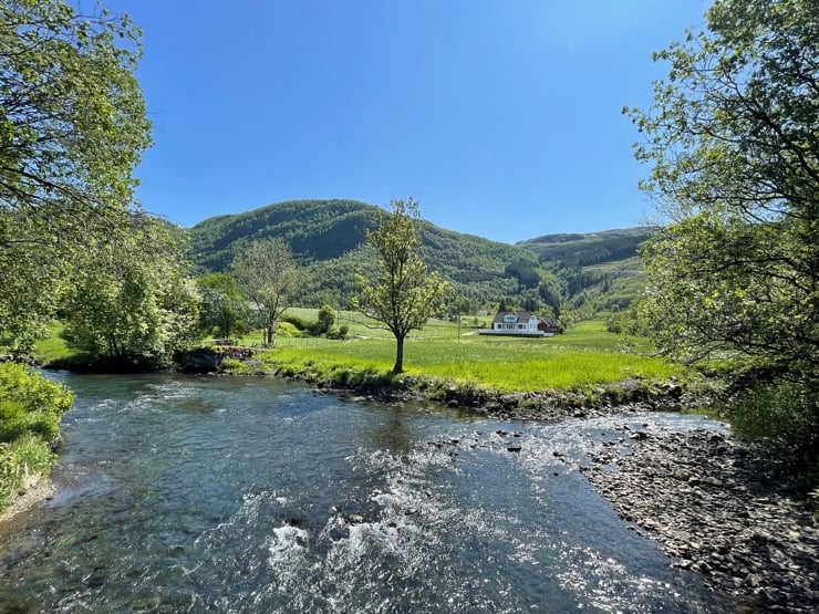 Blå himmel, skogkledde fjell, elveleie