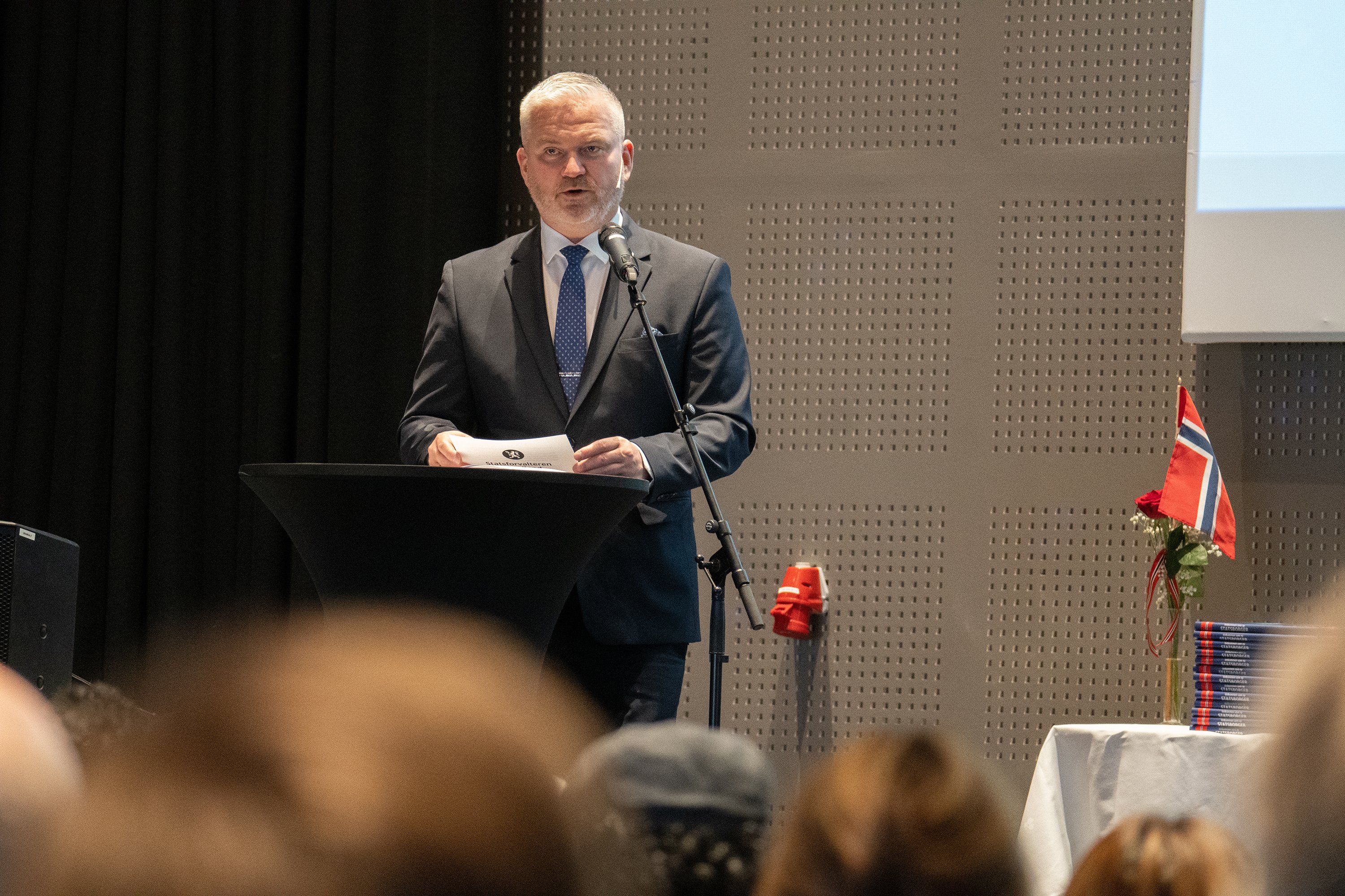 Statsforvalter Tom Cato Karlsen var en av dem som talte til de nye statsborgerne og gjestene. Foto: Emil Harjo Indsetviken / Statsforvalteren i Nordland. En mann i dress står foran en talestol.