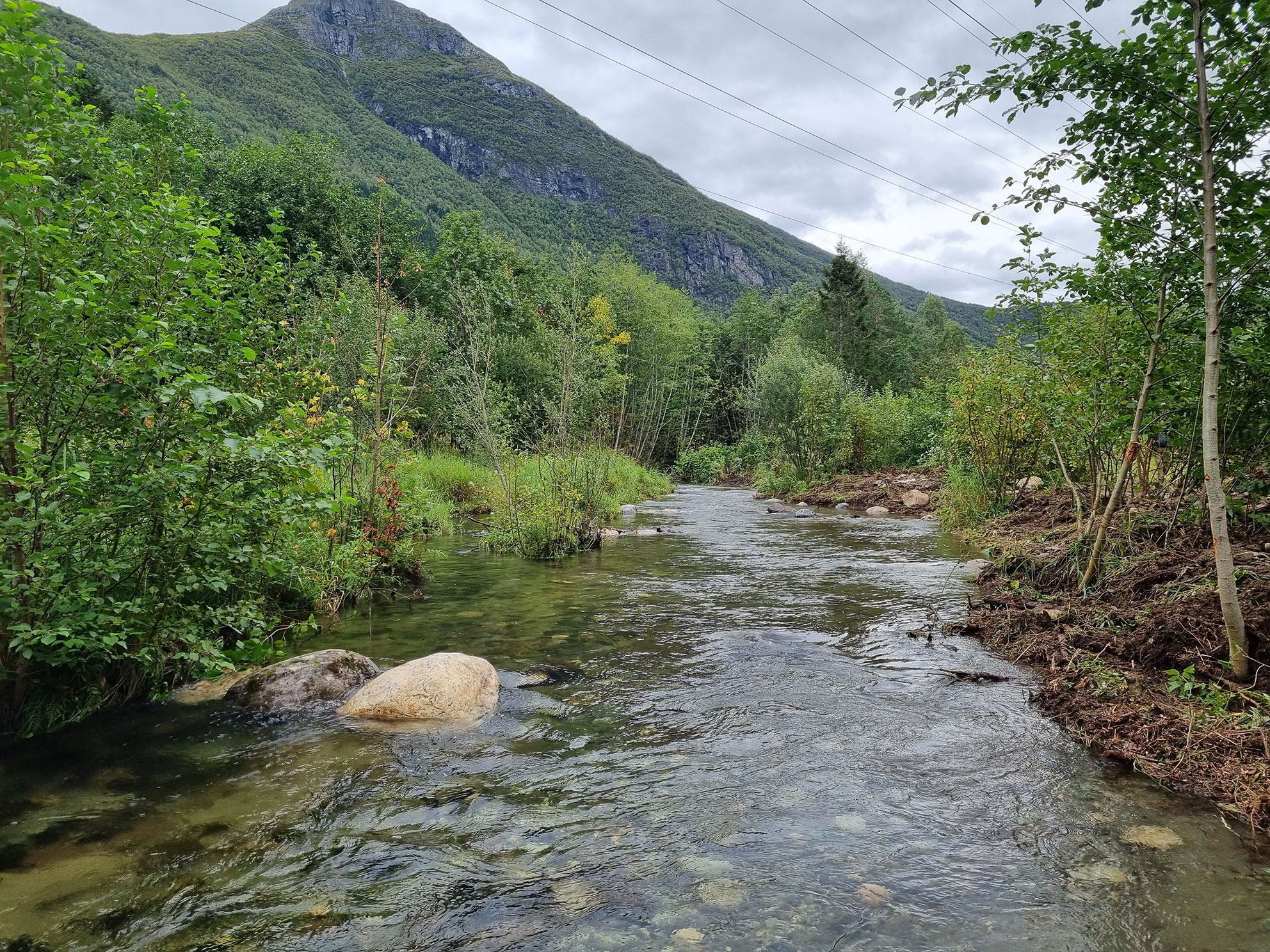 Ei brei elv med steinar i og med elvekantar som er rydda for vegetasjon.