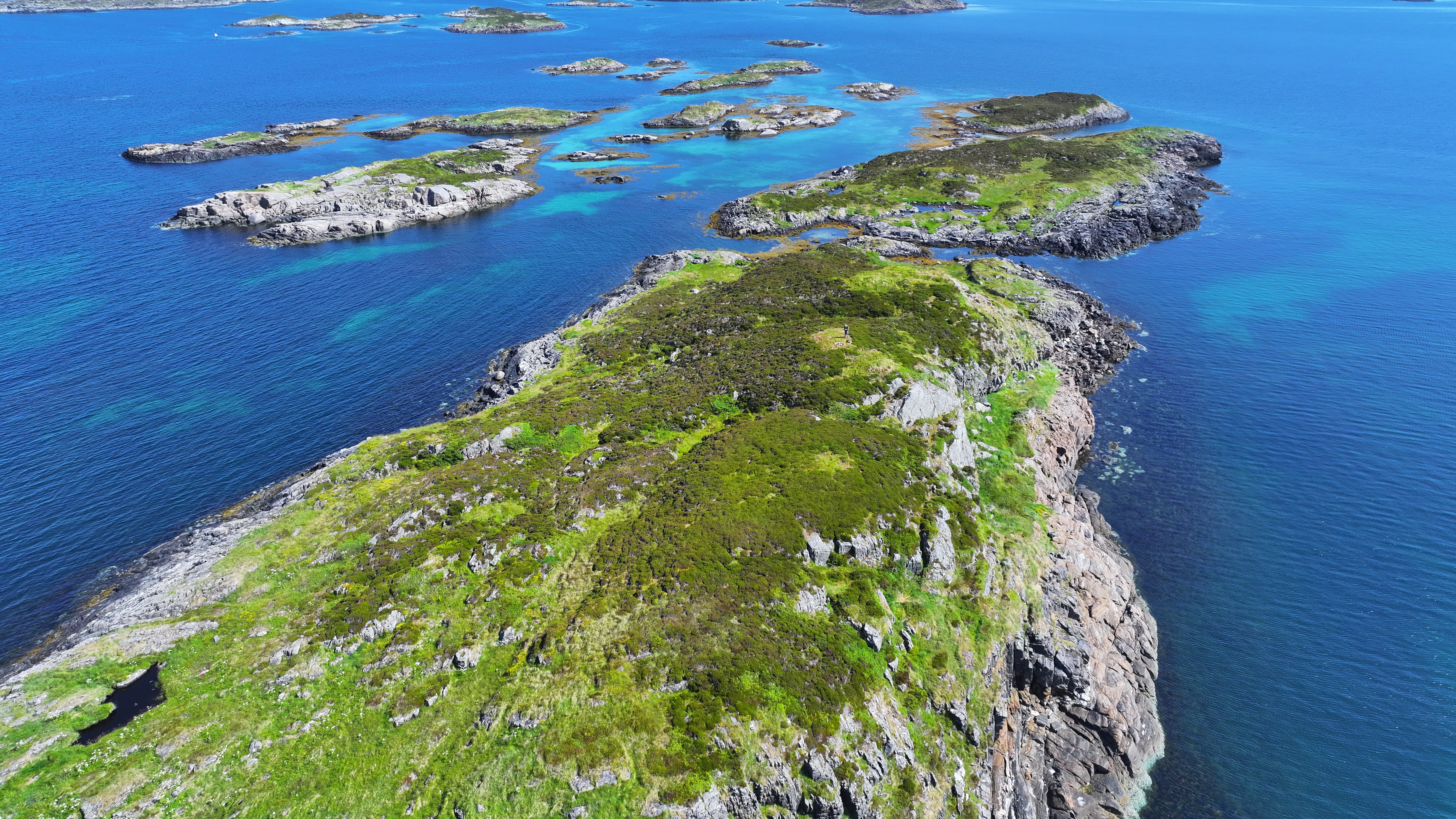 Holmar og skjer med grøn vegetasjon og blå roleg sjø rundt, sett frå lufta.