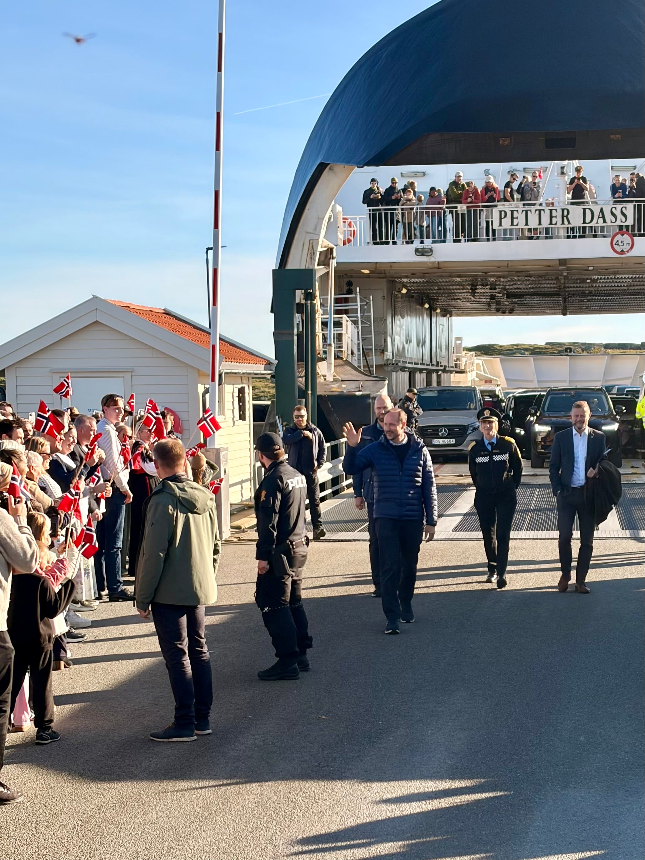 Kong Haakon blir ønsket velkommen på ferjekaien på Kvitsøy av ordføreren og blomsterbarn, med statsforvalter Bent Høie og politimester Gøril Våland i bakgrunnen.
