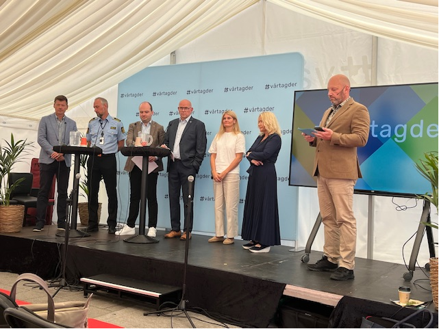 Fra venstre: Geir Ove Venemyr (Universitetet i Innlandet), Torgeir Winsnes (Agder politidistrikt), Sindre Lysø (Arbeiderpartiet), Yngve Årøy (Statsforvalteren i Agder), Ann Karin Fuglestad (Lyngdal kommune), Kristin Holm Jensen (KS) og Ronny Bjørnevåg (Lyngdal kommune). Foto: Birger Abrahamsen / Lyngdal kommune. Bilde av debattdeltagere og ordstyrer, med #vårtagder-logoer i bakgrunnen.