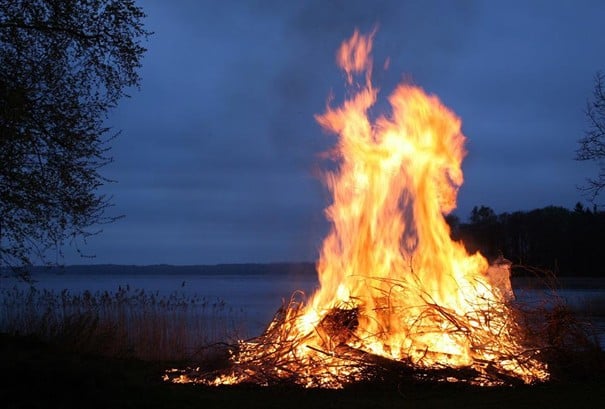 Stort bål bestående av kvister og trevirke, foran en innsjø, på kveldstid. Kilde: pixabay.com