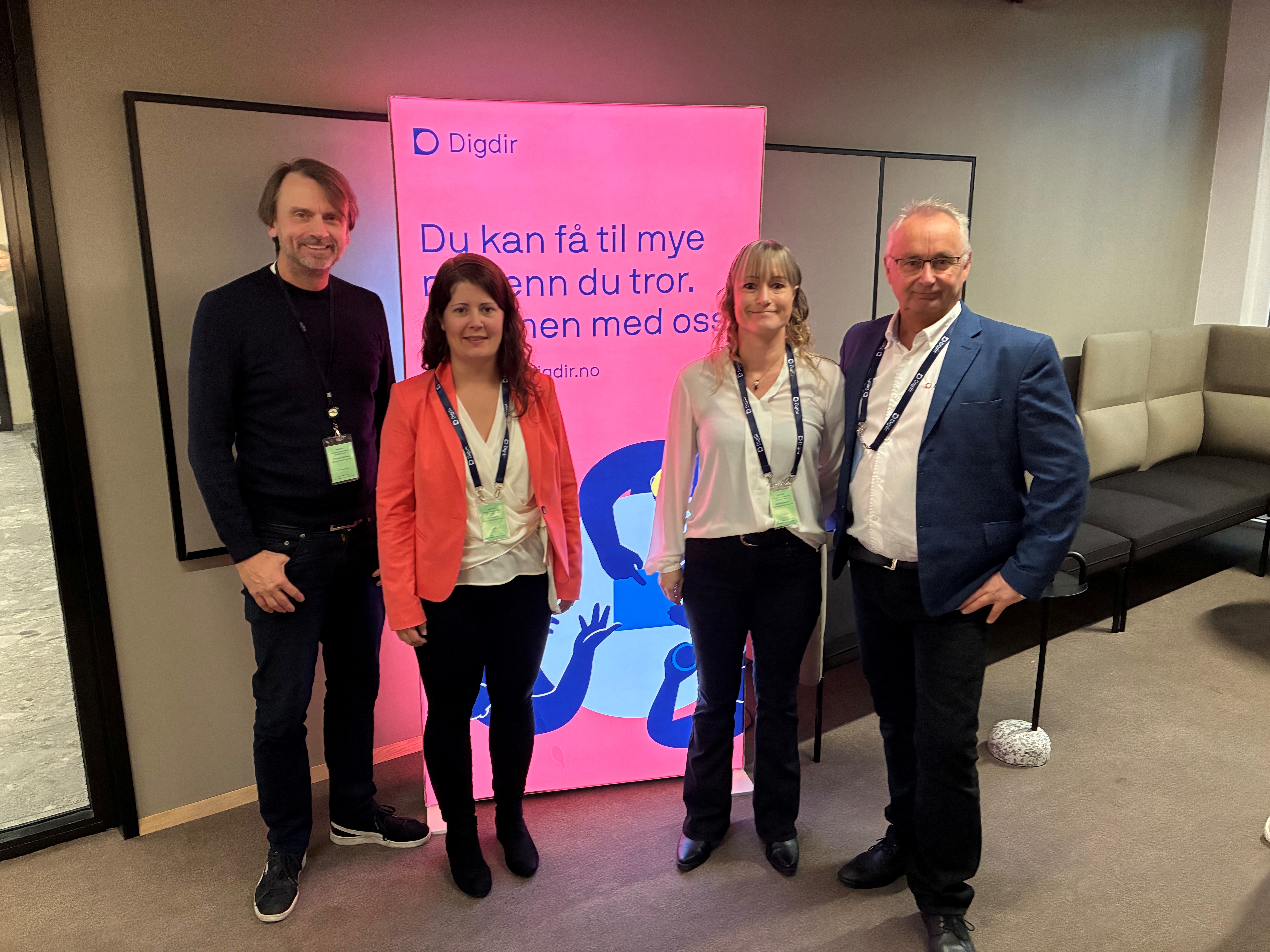 Gruppebilde av to ansatte i Digdir og to ansatte i STAF foran en rosa Digdir-rollup.