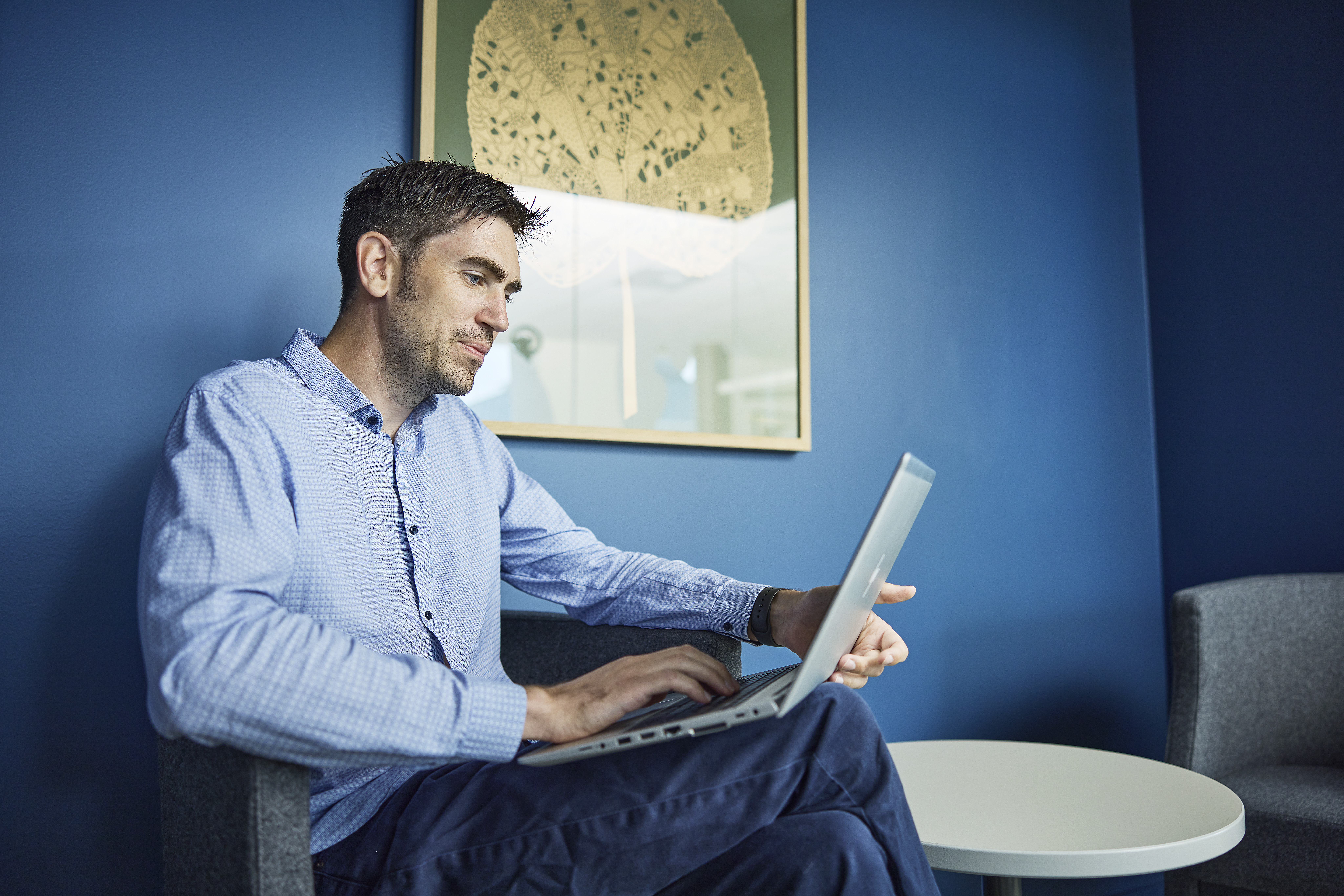 Mann sitter og jobber avslappet på en laptop