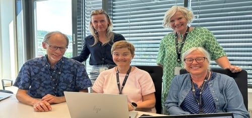 Fem ansatte som står rundt en lap-top