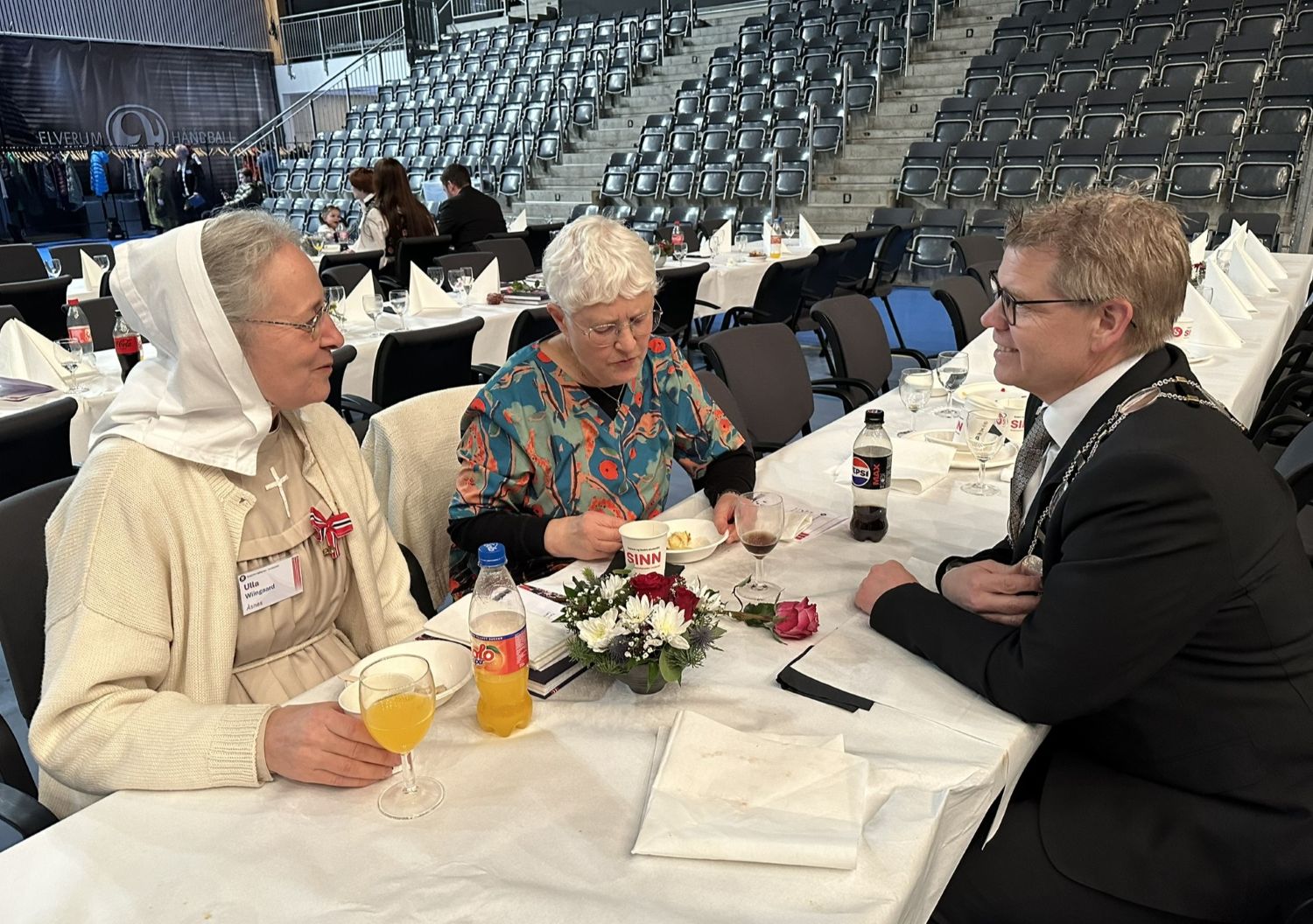 To kvinner og en mann sitter ved et bord og snakker sammen