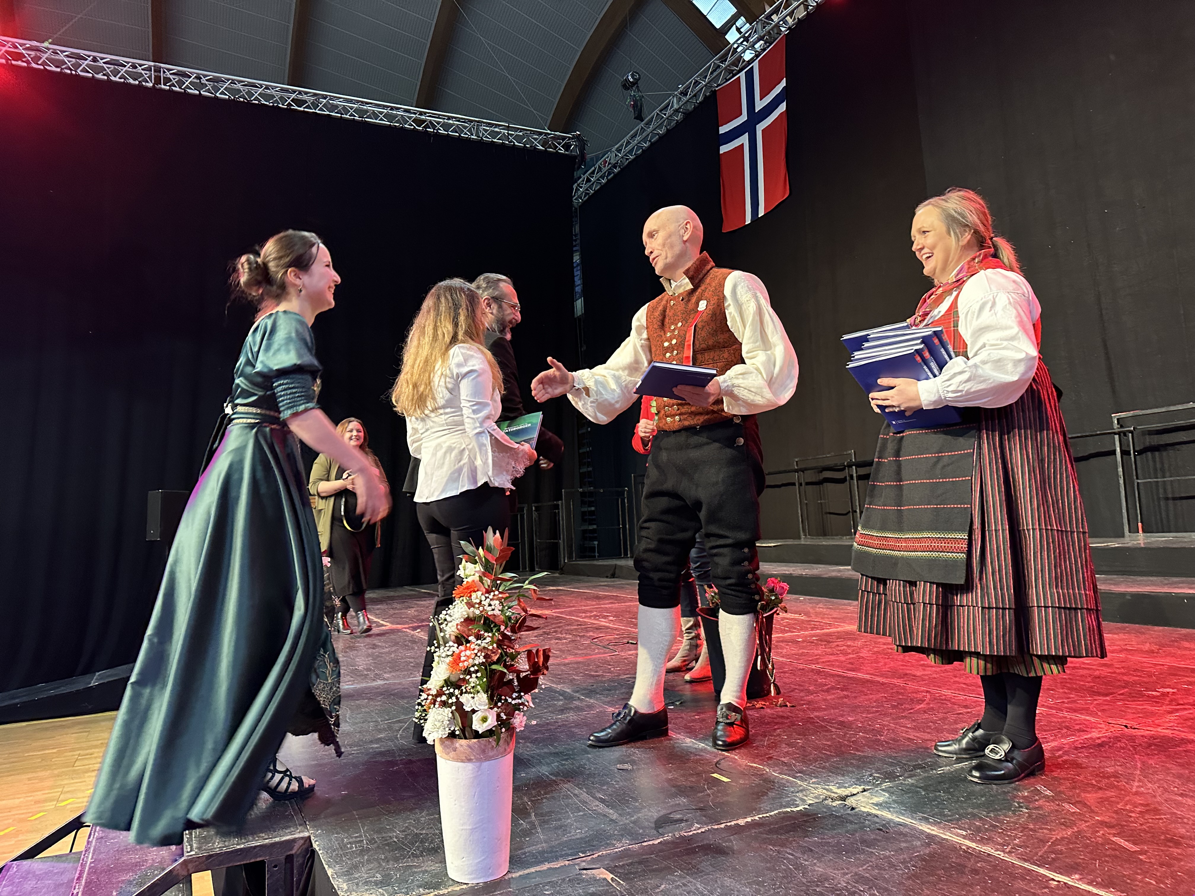 Nye statsborgere fra Sel kommune tas i mot av statsforvalter Sigurd Tremoen. Foto: Karianne Stordal. Statsborgere kommer på scenen under seremoni, og statsforvalter håndhilser.