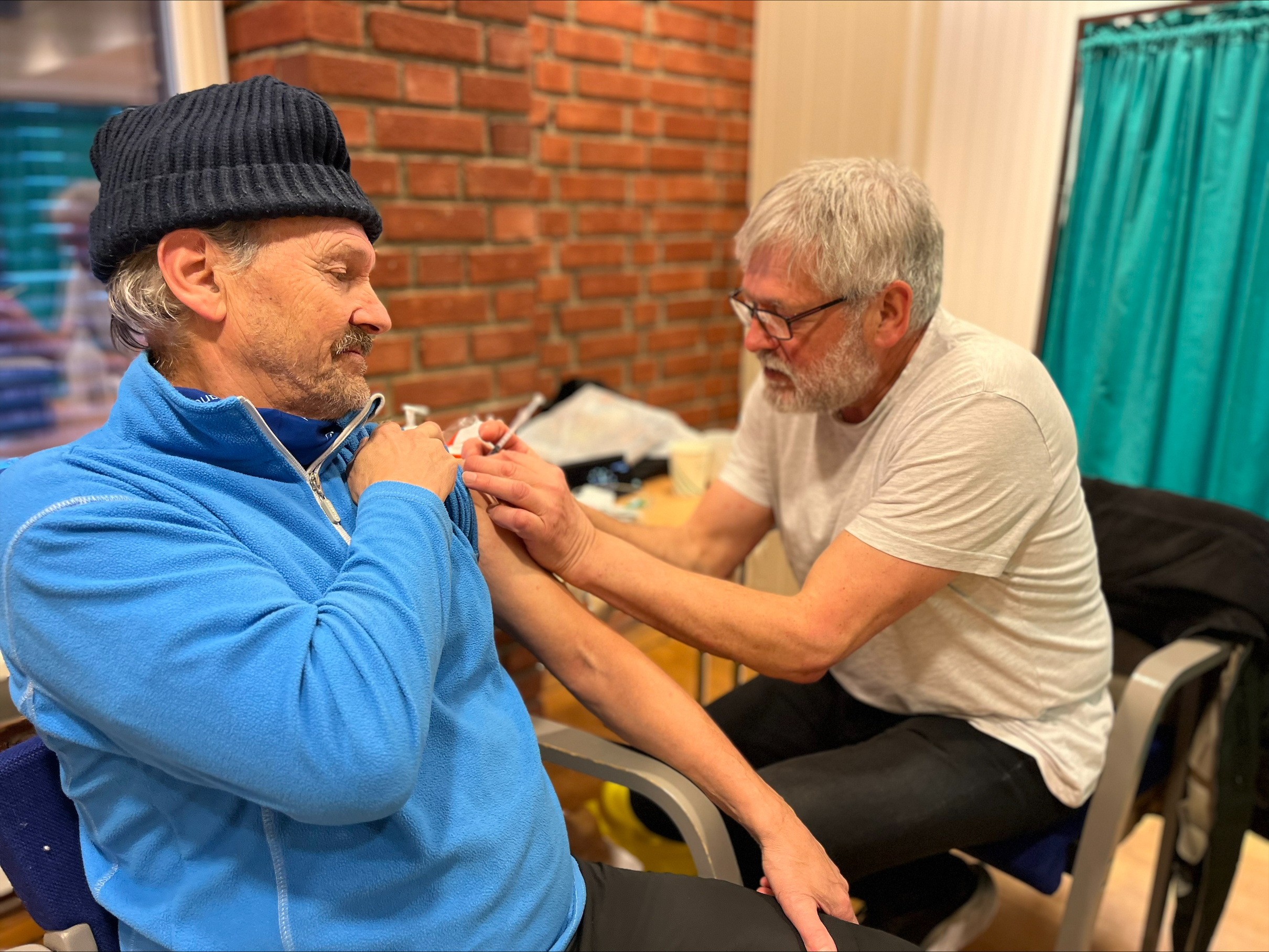 Knut Torgersen fra Follebu får dagens første vaksine av frivillig sykepleier Tony Heyerdahl. Foto: Ragne Stauri. En mann får vaksine av sykepleier.