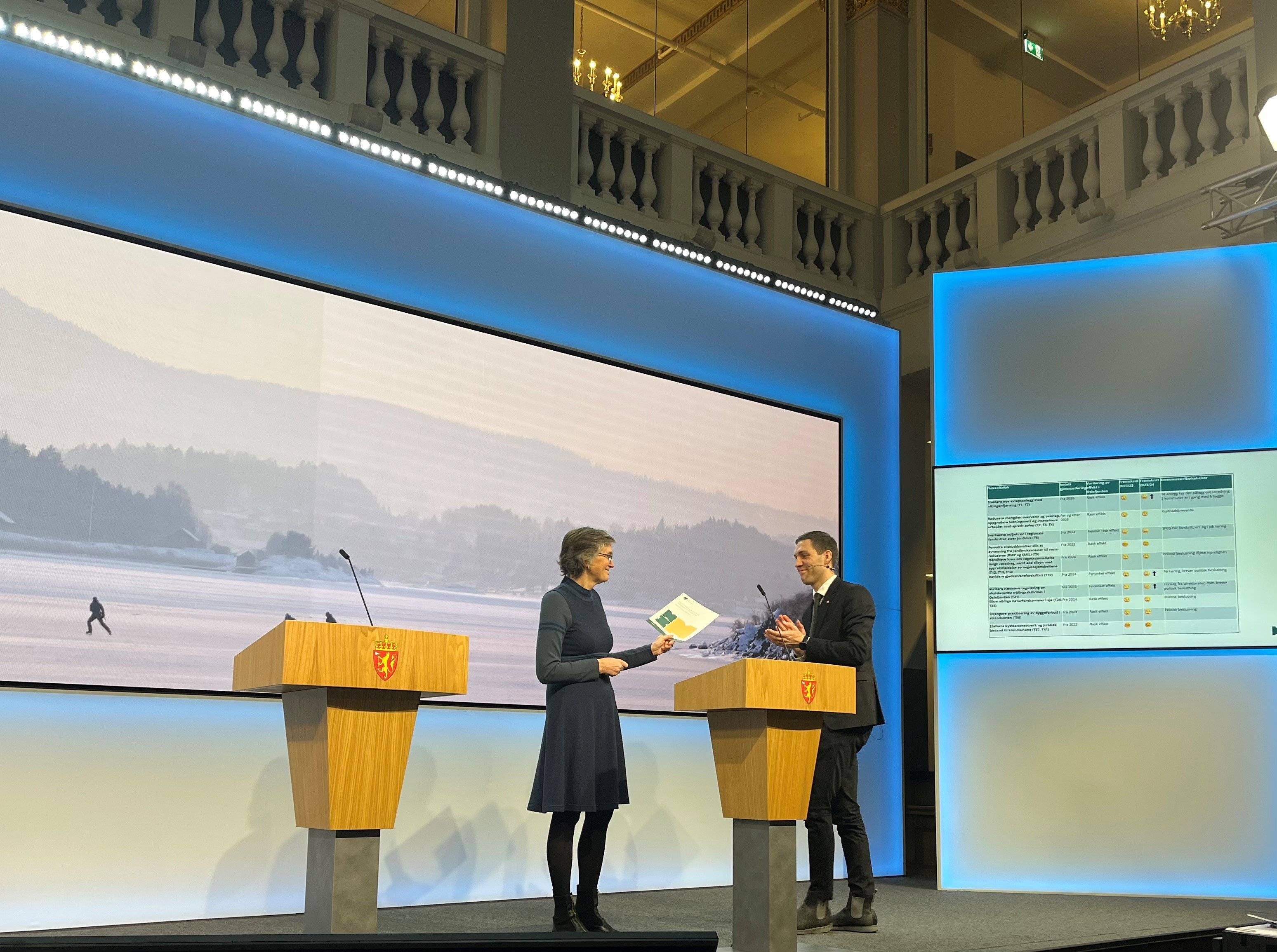 Direktør i Miljødirektoratet Ellen Hambro overrekker tredje statusrapport til klima- og miljøminister Andreas Bjelland Eriksen. Foto: Sigrid Hårstad Pålsrud Dame som overrekker en rapport til en mann.