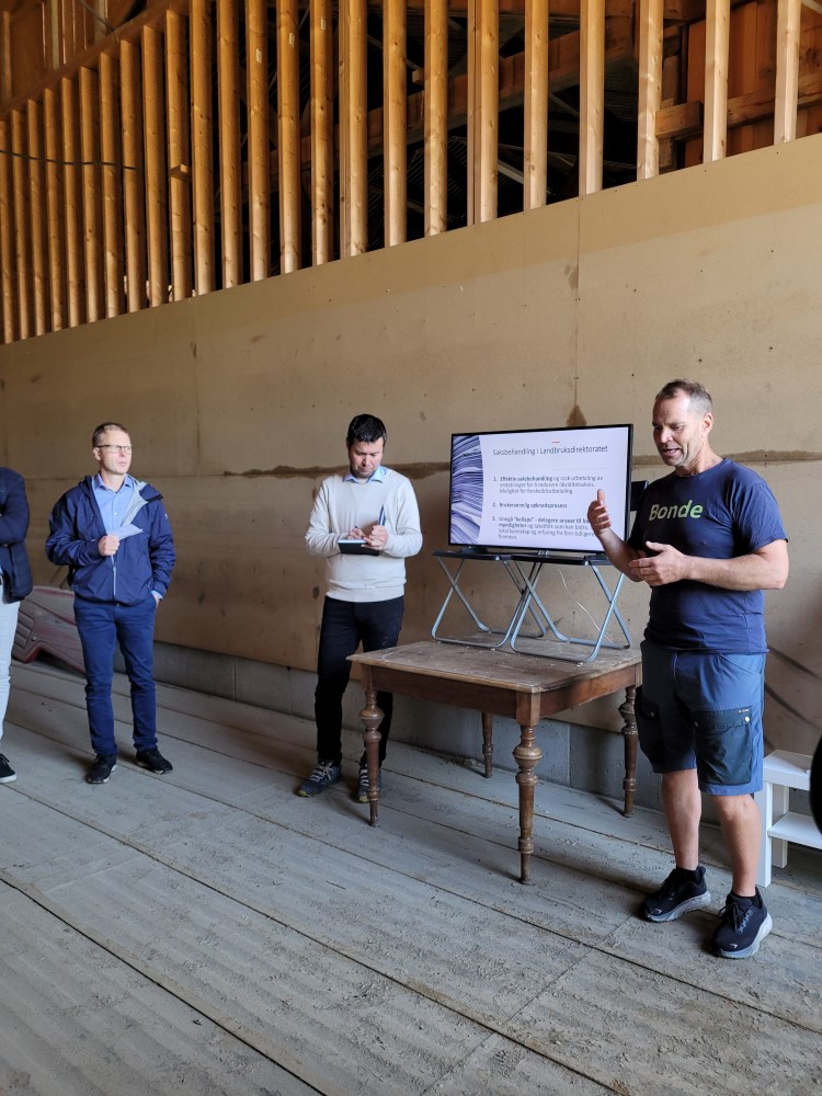 Landbruks- og matminister Geir Pollestad (i midten), Knut Evensen frå Fåvang Bondelag (til høgre) og ordstyrar Øyvind Gotehus frå Statsforvaltaren (til venstre). Foto: Anne Berit Grasbakken. Bilde av tre menn i ei korntørke. Landbruks- og matministeren lyttar og noterer til innlegg frå ein bonde, medan møteleiaren følger med.