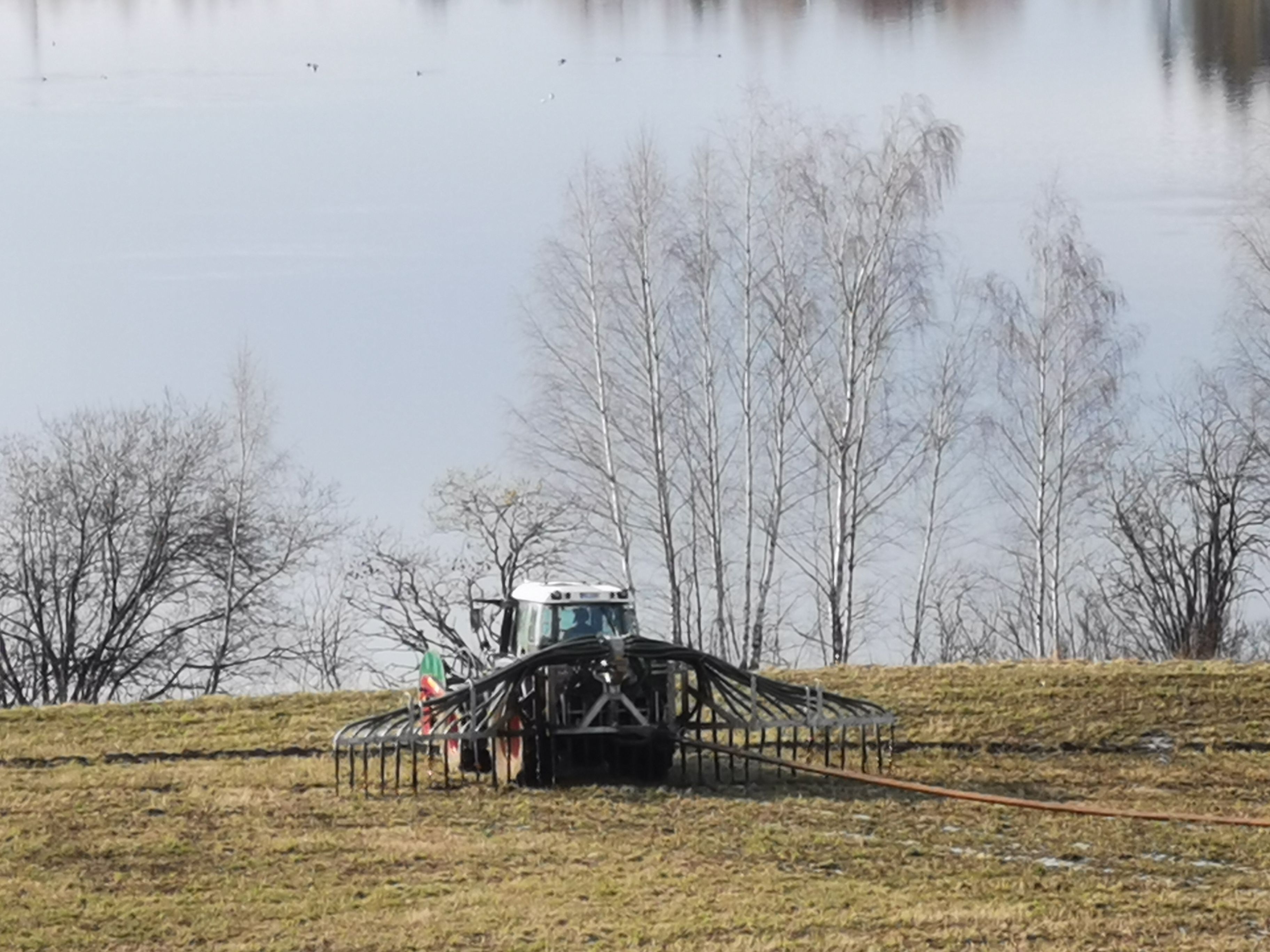 Traktor som legger ned husdyrgjødsel med bom og tilførselsslange på åker med vannspeil i bakgrunnen