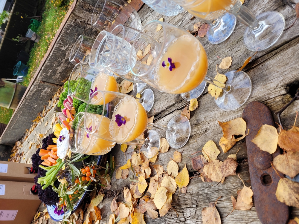 Stettglass med eplemost, pynta med stemorsblomst. I bakgrunnen fat med grønnsaker.