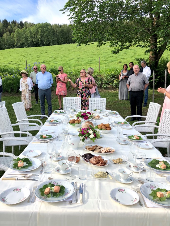 Hageselskap på Simenstad Foto: Turid Windjusveen Olsen. Mennesker som står bak et dekket bord ute i en hage