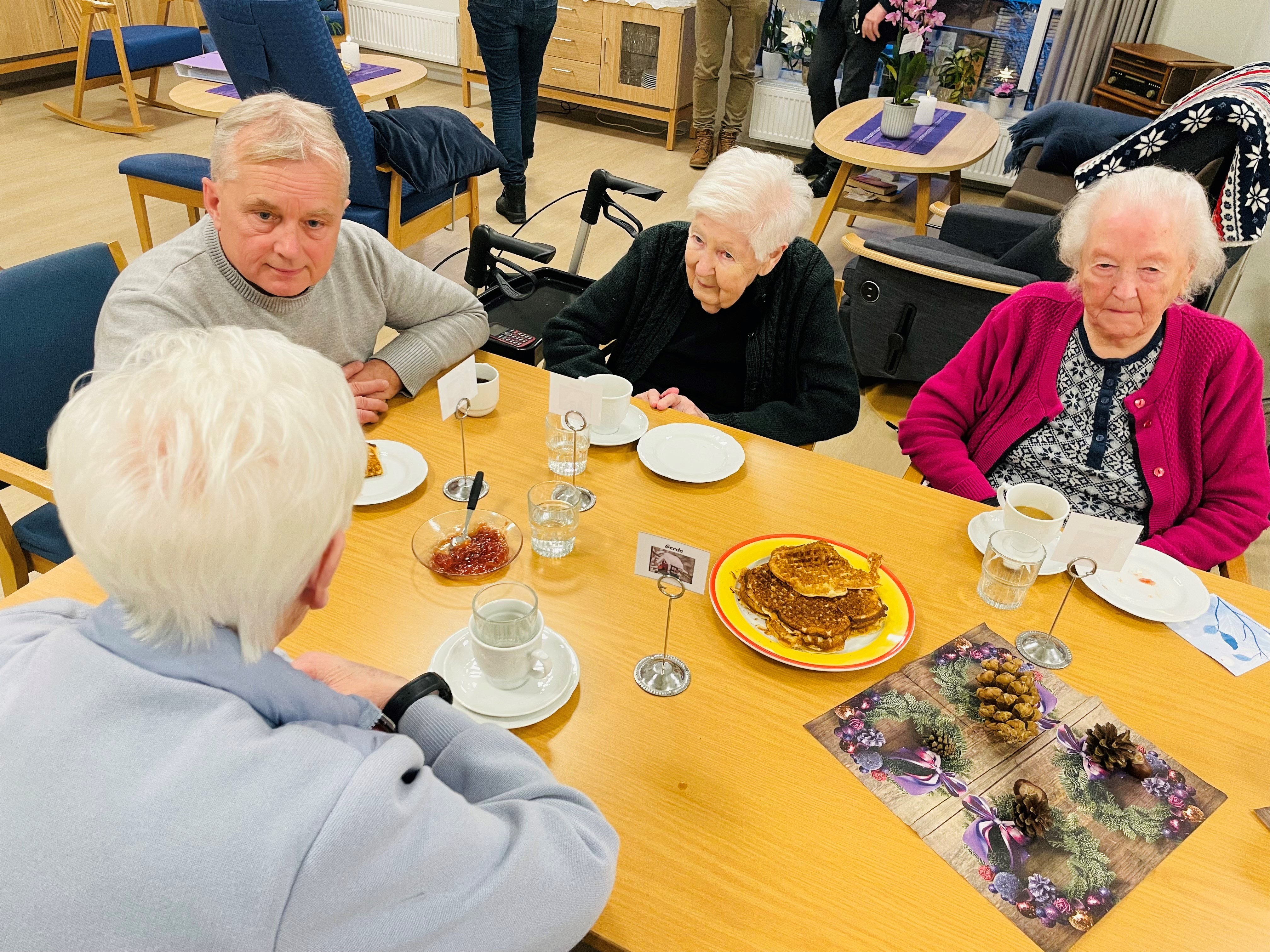 Knut Storberget i samtale med brukerne på Labo. I dag er det vaffeldag. Foto: Kristina Skamsar. Mann i samtale med eldre mennesker rundt et bord på en institusjon.