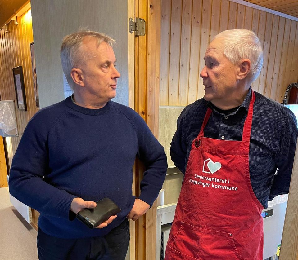 Statsforvalter møter kjøkkenforvalter på Seniorsenteret. Foto: Line Gabrielsen Brovold / Statsforvalteren i Innlandet. Knut Storberget står i døra til kjøkkenet på seniorsenteret sammen med eldre frivillig mann i rødt forkle,