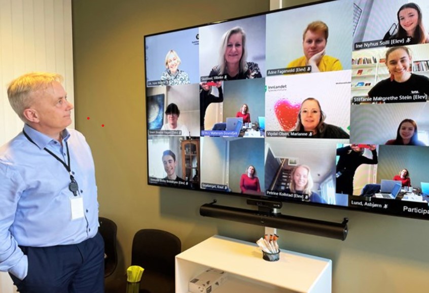 Mann som står fremfor en skjerm som viser digitale møtedeltakere
