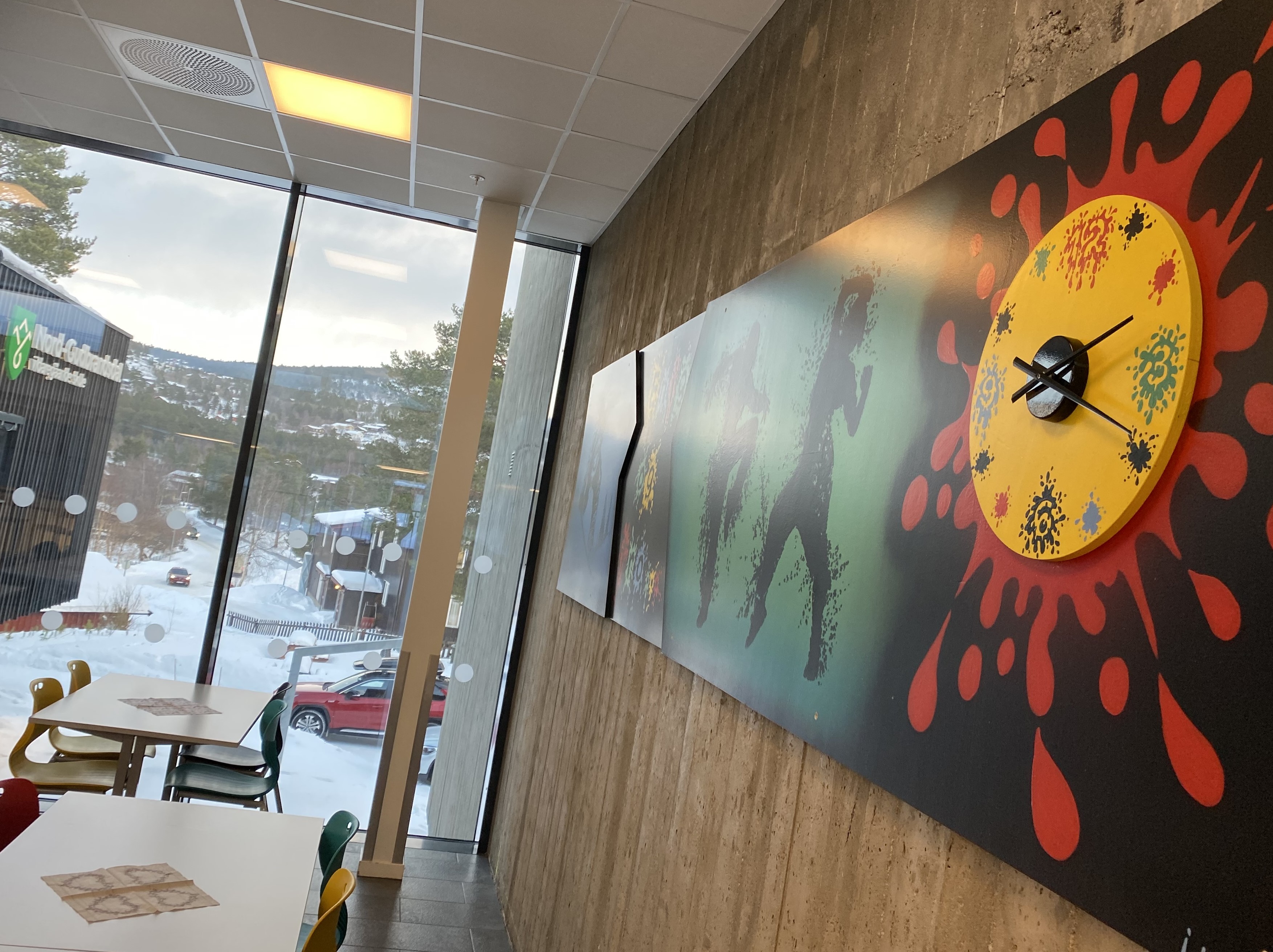 Skolen er et pulspunkt i Dovre kommune, og på Dombås er både ungdomsskolen og videregående samlet i moderne lokaler. Foto: Karianne Stordal / Statsforvalteren i Innlandet. Et fargerikt bilde som henger på veggen på den videregående skolen på Dombås, med fjellene synlig utenfor vinduene.