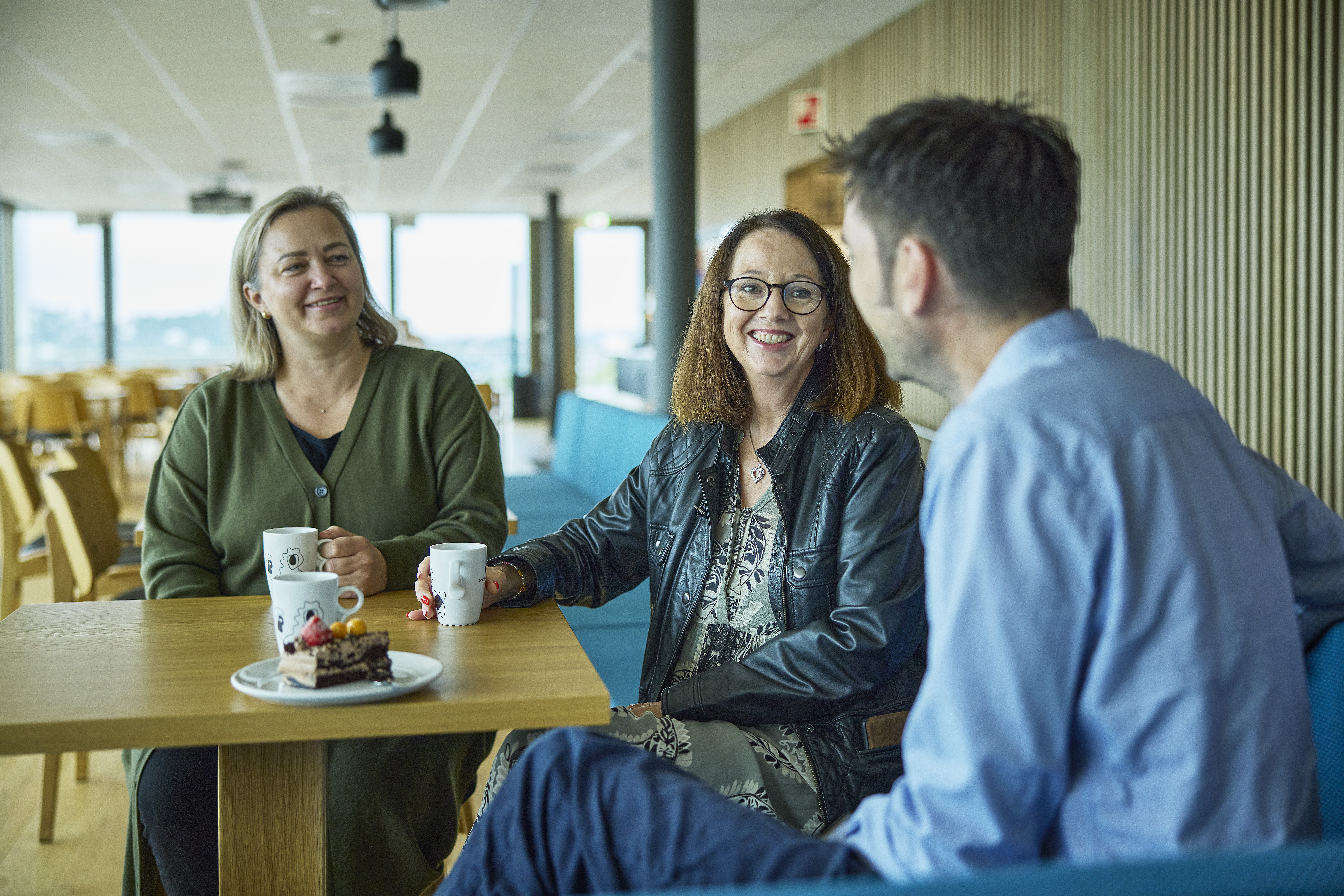 Tre kollegaer sitter i kantinen og har kaffe